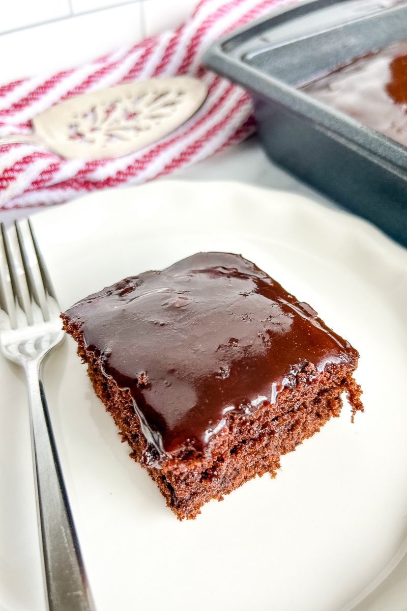 A slice of chocolate cake on a white plate with a fork.