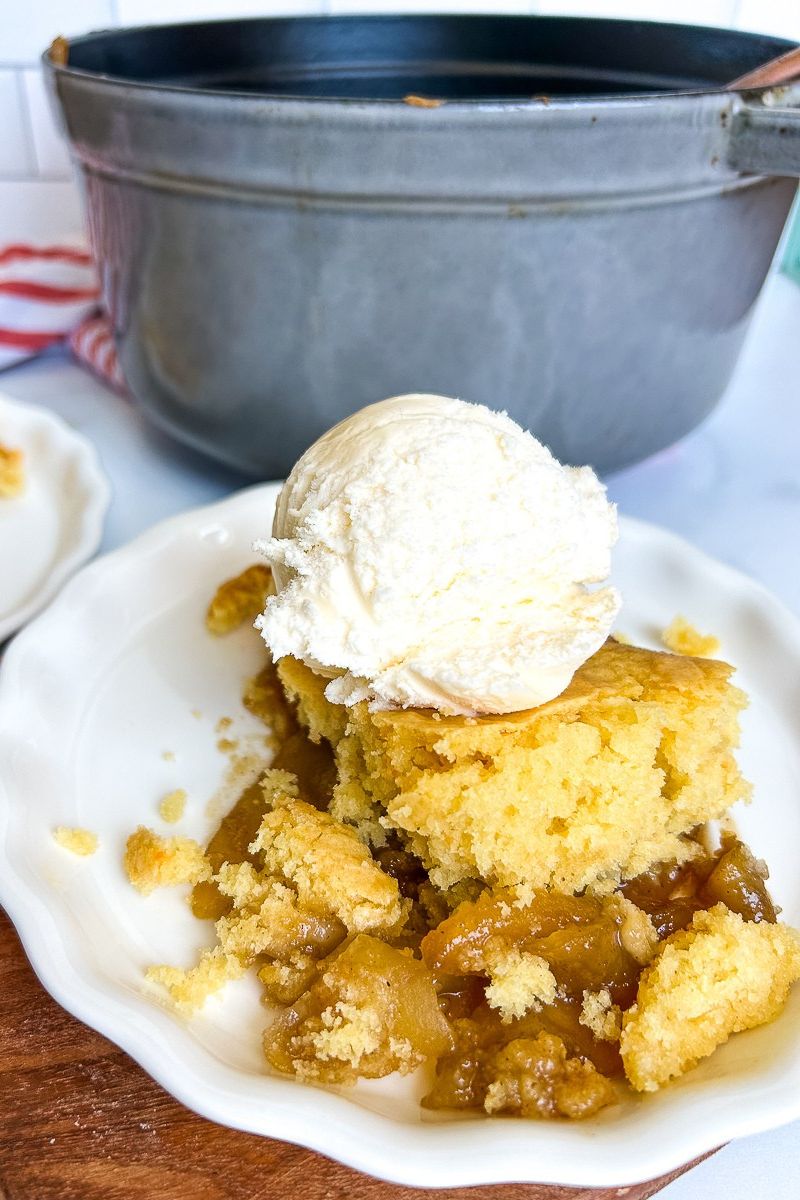A serving of apple cobbler with vanilla ice cream on a white plate.