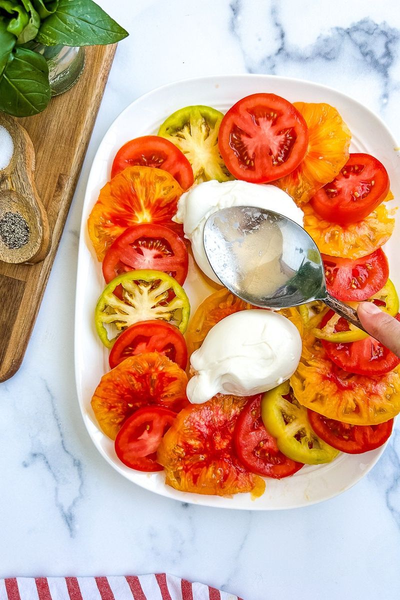 Sliced tomatoes on a white serving plate with burrata in the middle.