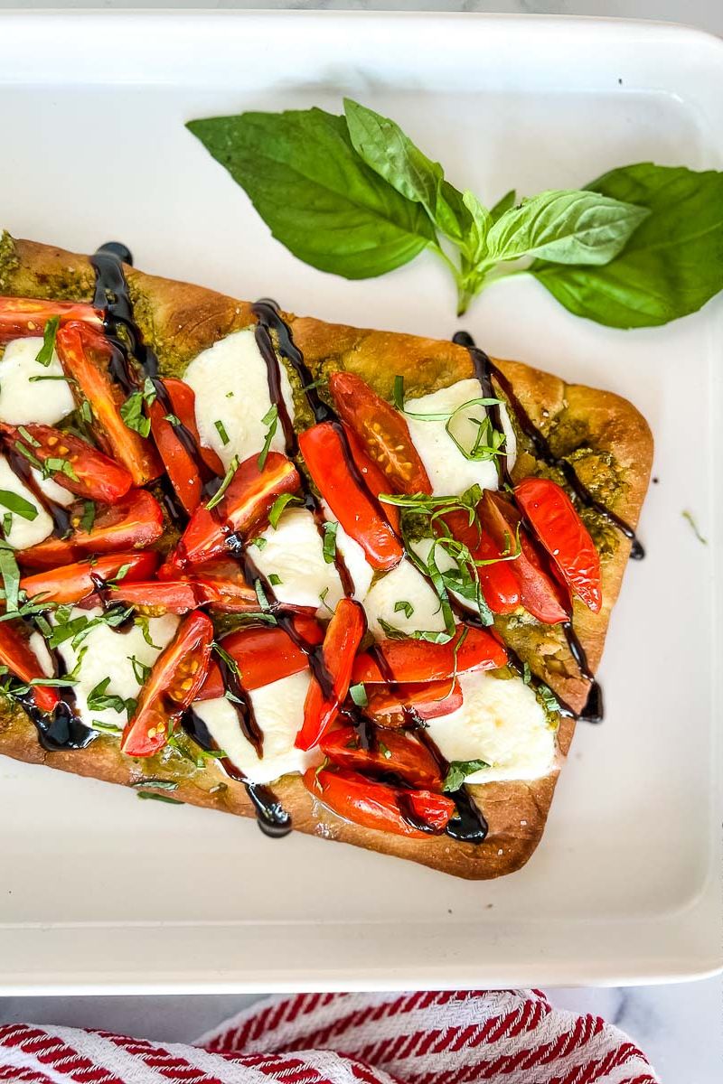Caprese flatbread with garnish on a white platter and basil leaves.