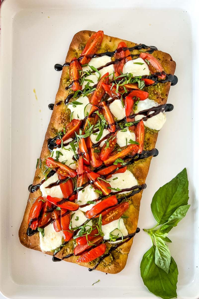 Caprese flatbread with garnish on a white platter and basil leaves.