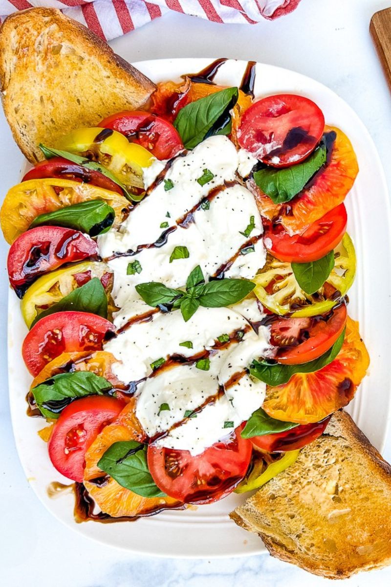 Burrata caprese on a white serving plate with slices of toast.