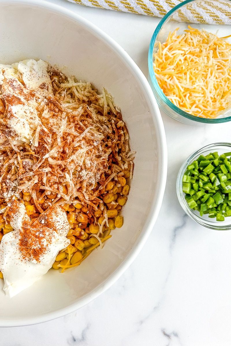 A bowl of mixed ingredients for corn dip and a bowl of cheese and chopped jalapenos.