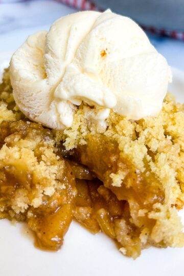 A serving of apple cobbler with vanilla ice cream on a white plate.