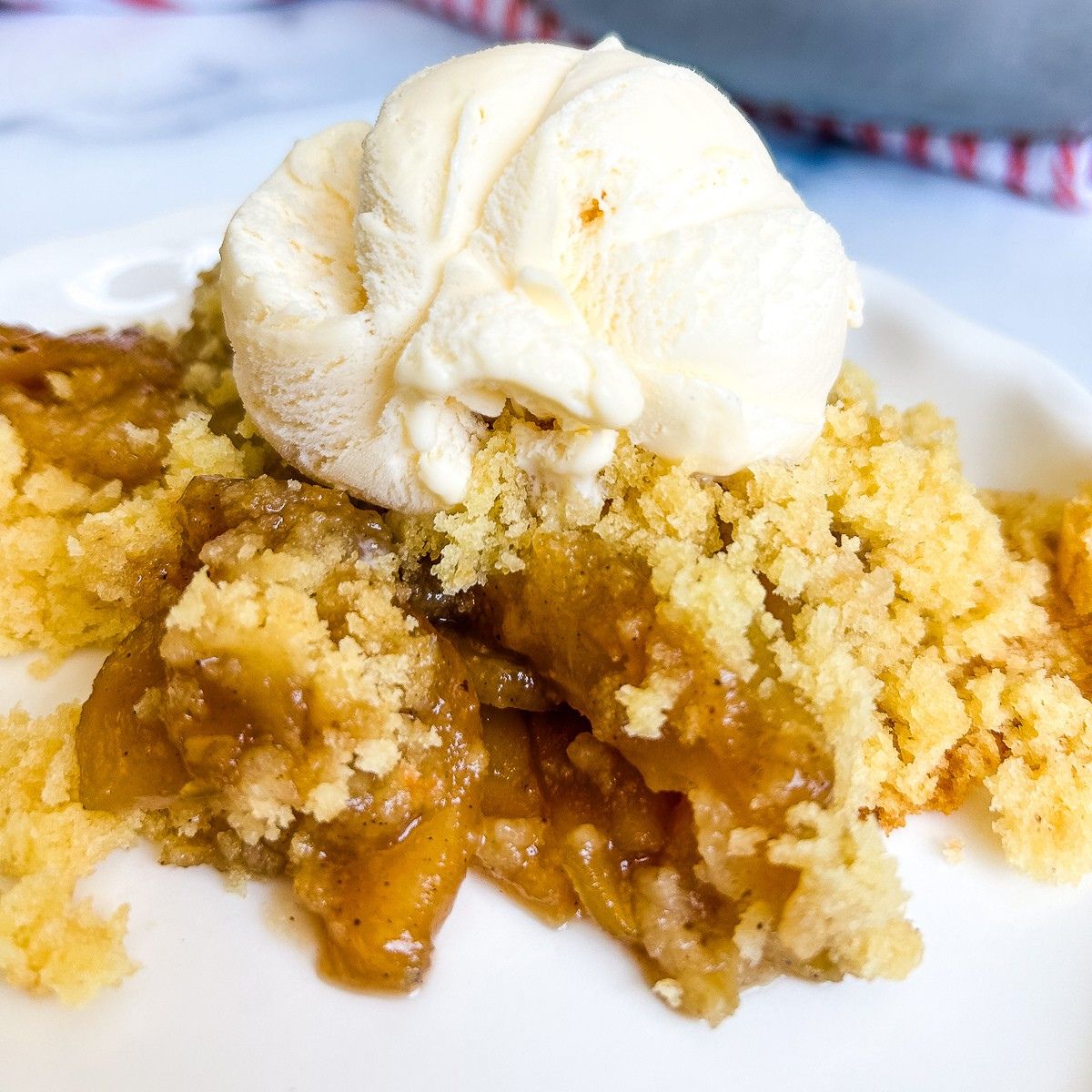 A serving of apple cobbler with vanilla ice cream on a white plate.