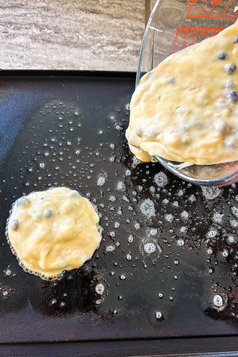 Blueberry pancakes are cooked on the griddle.