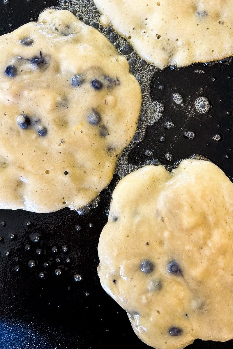 Blueberry pancakes are cooked on the griddle.