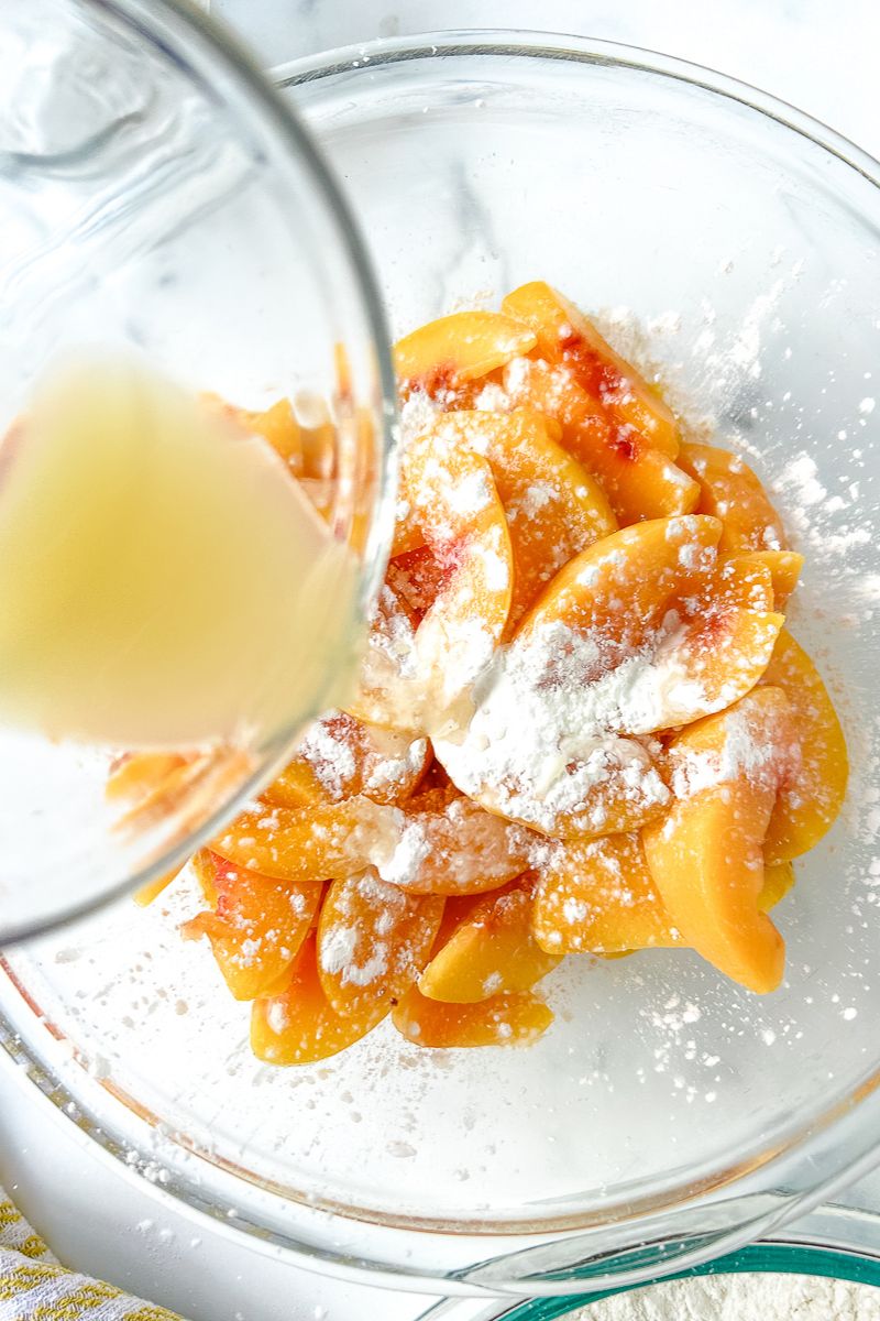 A bowl of juice being poured into a bowl of peaches with powder.