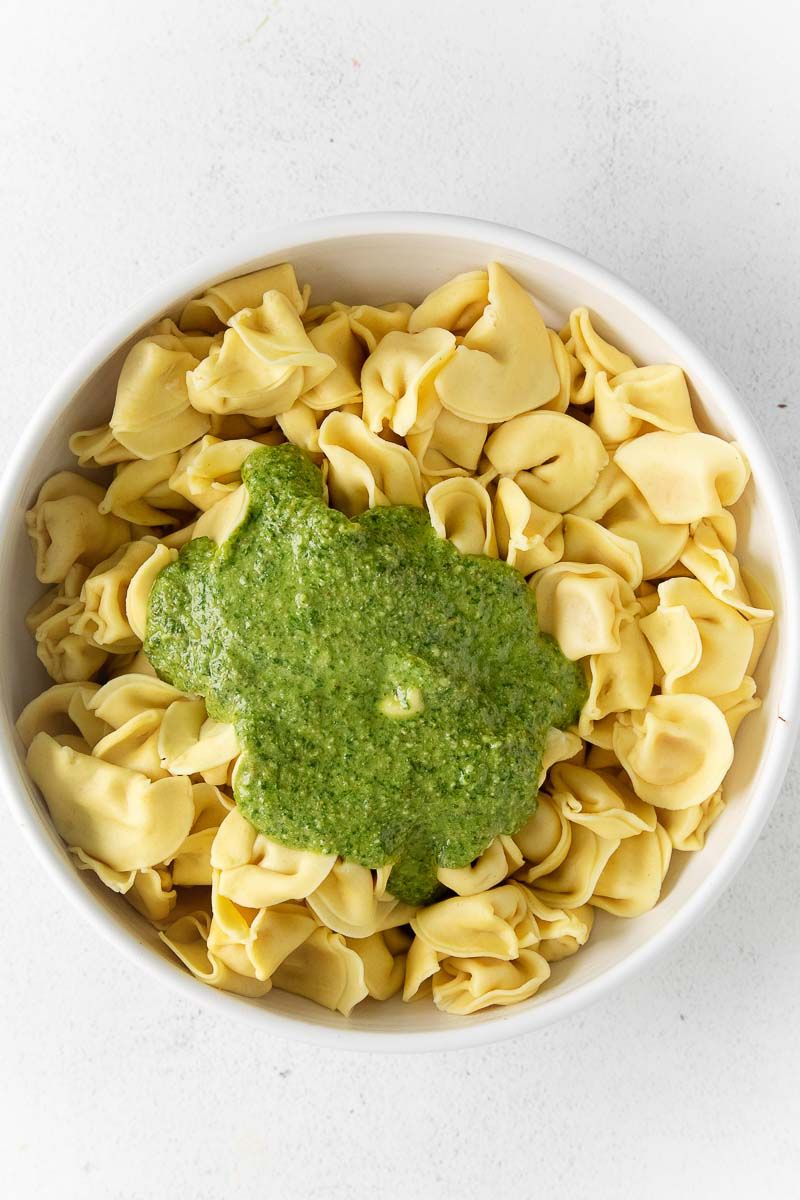 A bowl of tortellini with a pesto sauce on top.
