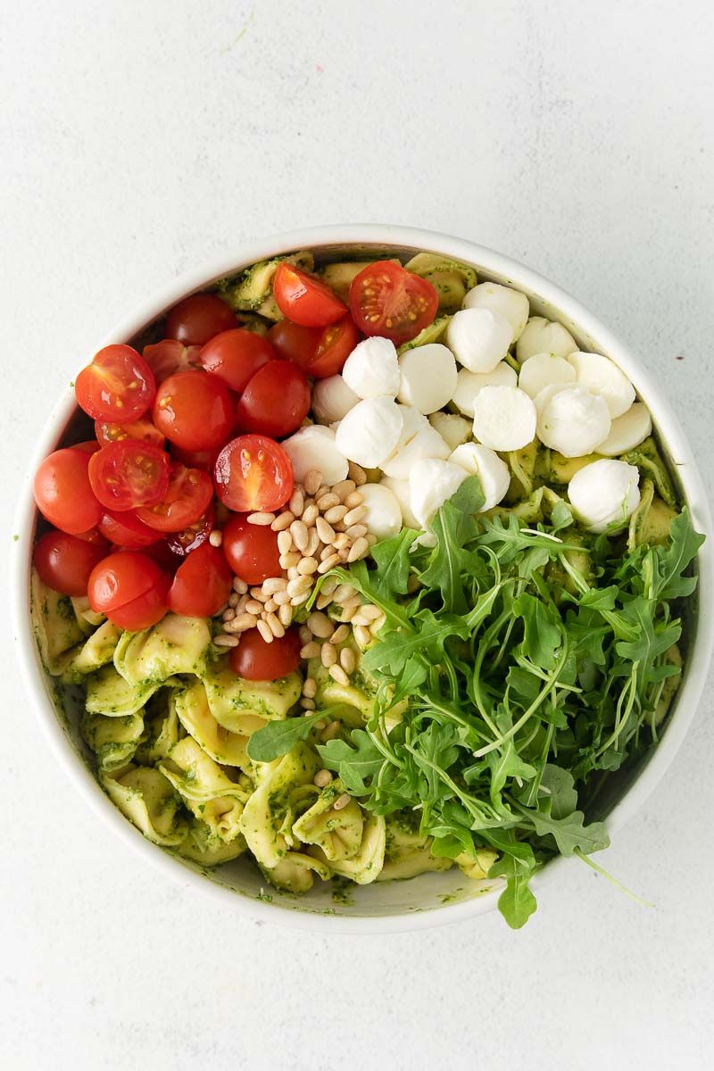A bowl with tomatoes, mozzarella, and other ingredients for pesto with tortellini.