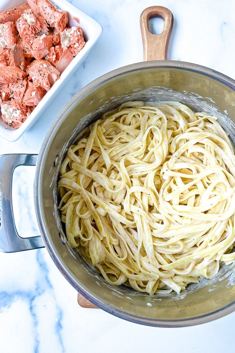 A platter of salmon and an pan of alfredo pasta.