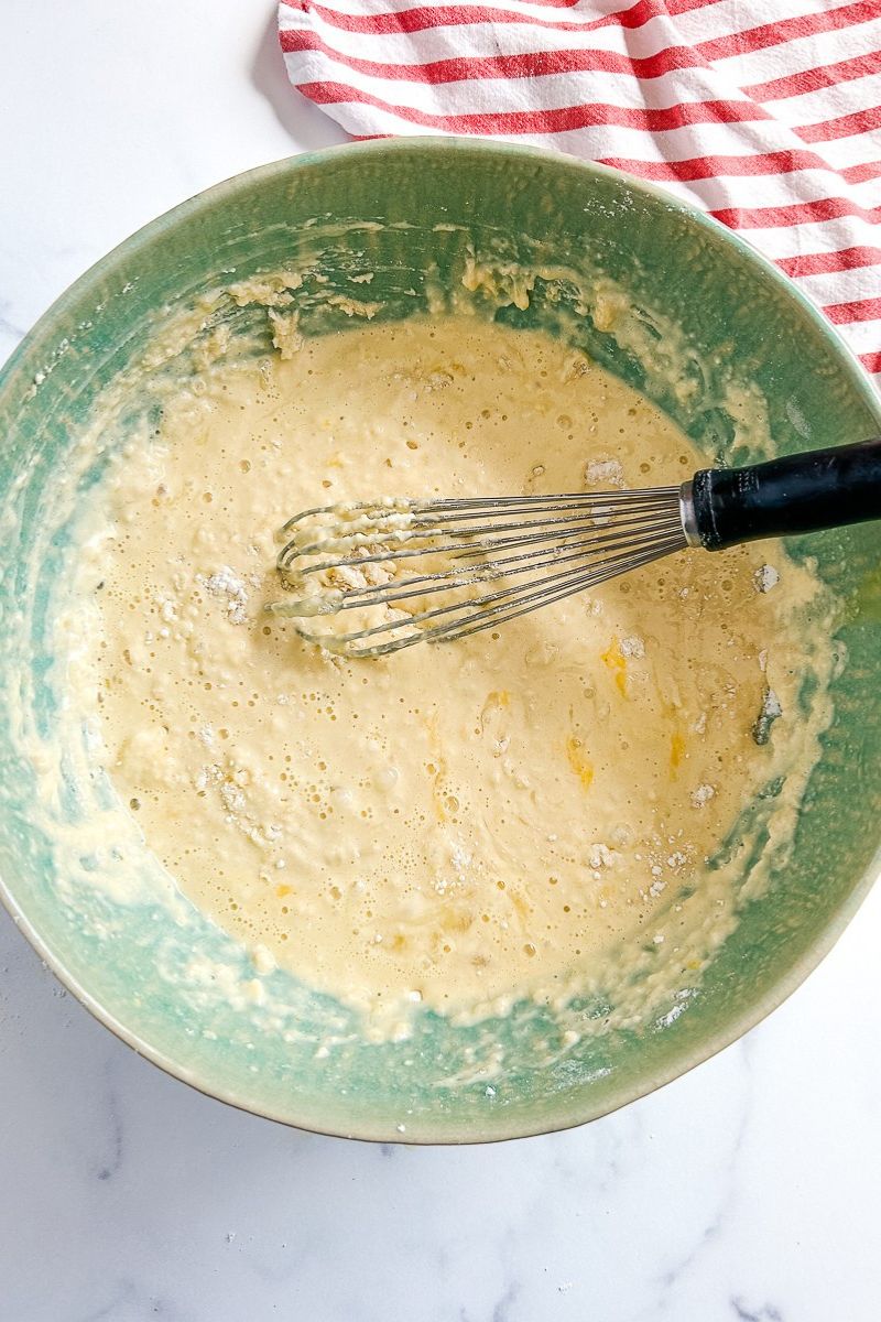 A batter of pancake in a green bowl with a whisk.