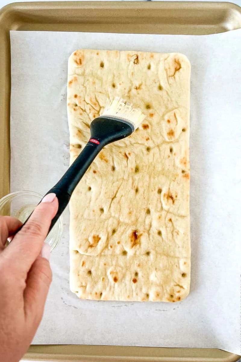 Brushing the flatbread with oil on a baking sheet.