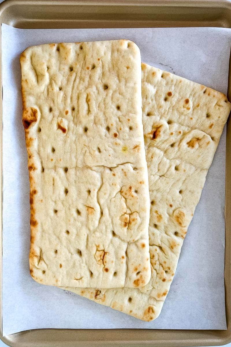 Two pieces of flatbread on a baking sheet with parchment paper.