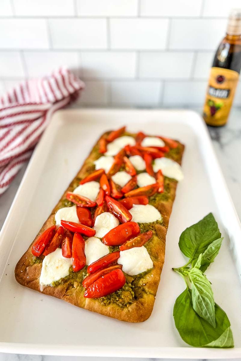 A flatbread on a baking sheet topped with cheese, tomatoes, and pesto sauce.