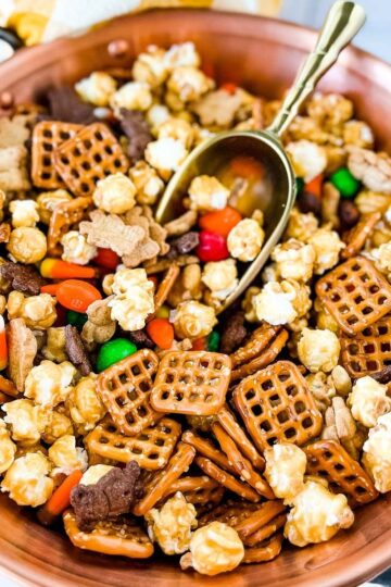 A bowl of snack mix for Halloween with a scoop.