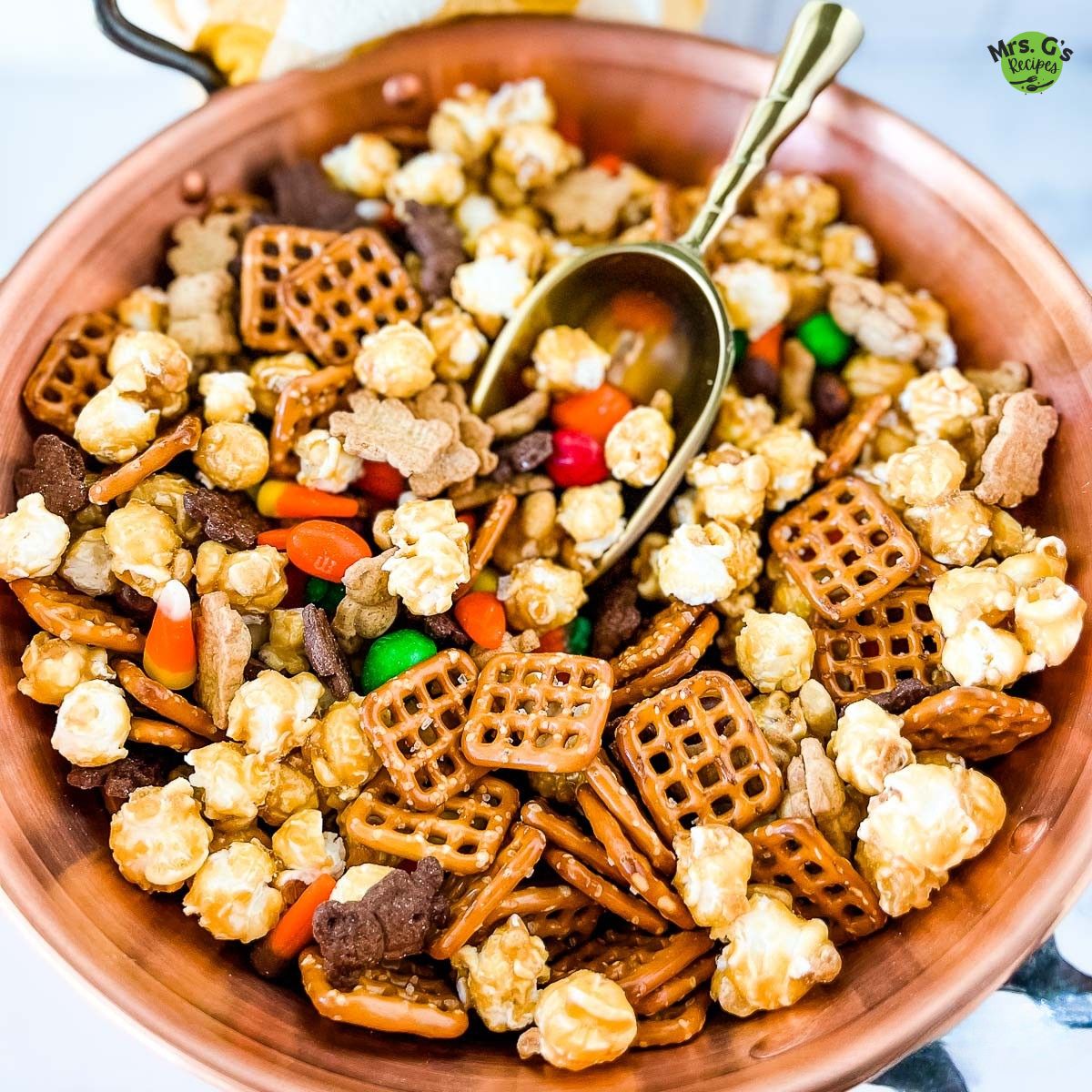 A bowl of snack mix for Halloween with a scoop.