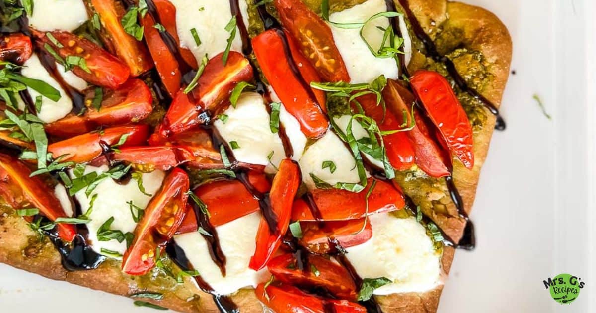 Caprese flatbread with garnish on a white platter and basil leaves.