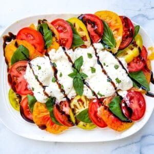 Burrata caprese on a white serving plate.