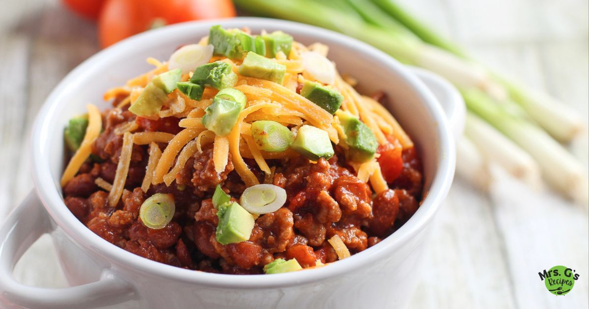 A bowl of chili with cheese and garnish on top.