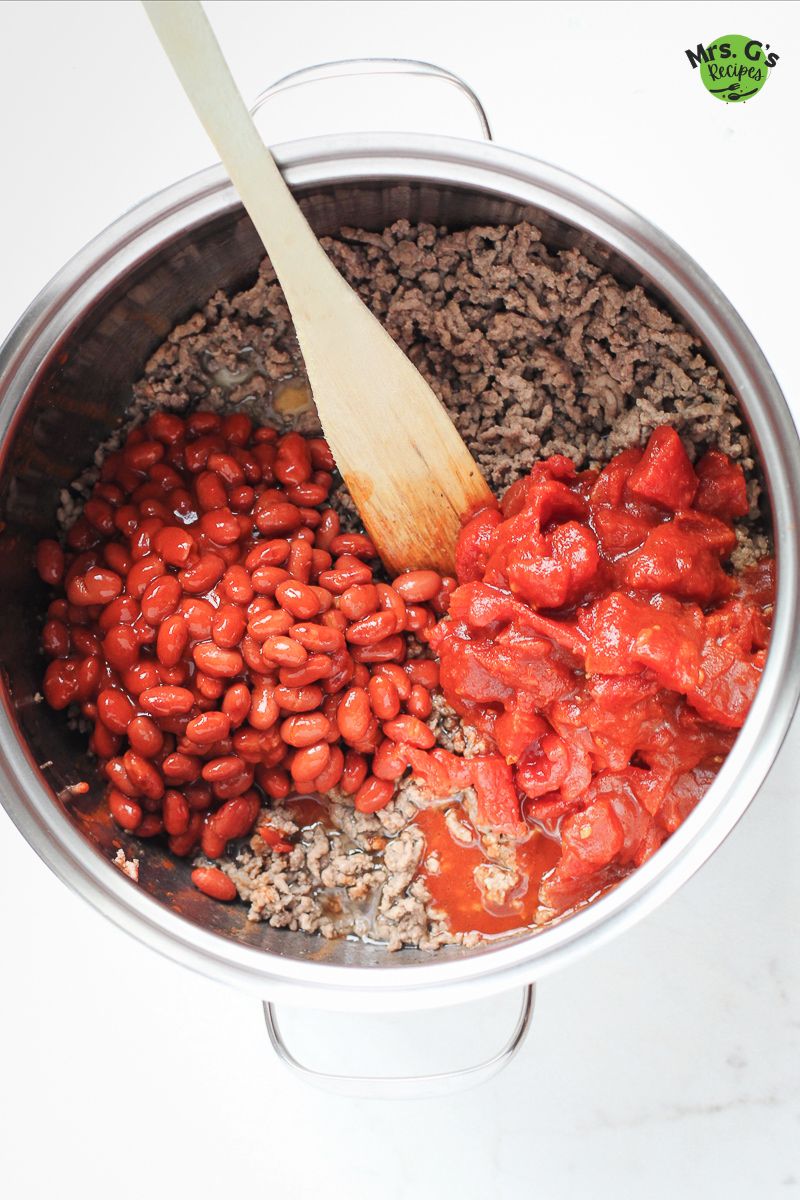 A pan with beans, ground meat, and sauce with a wooden ladle.