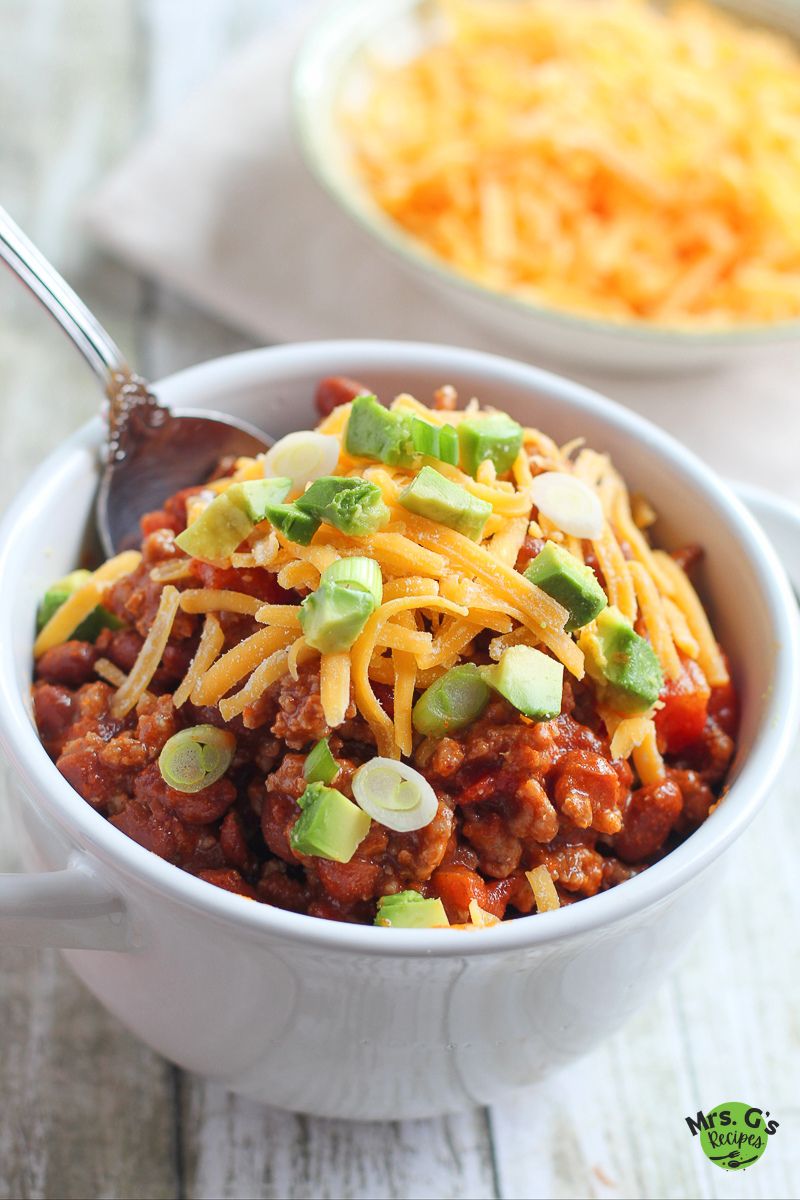 A bowl of chili with cheese and garnish on top.