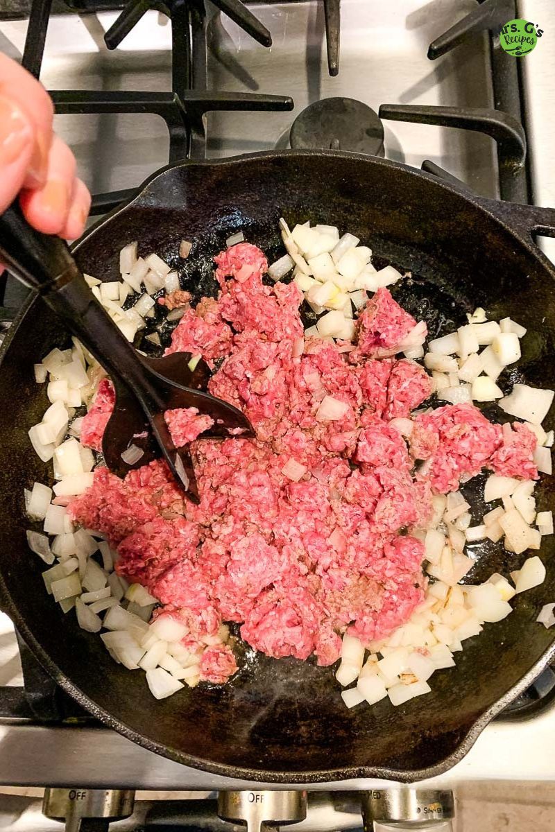 A skillet of meat and onions with meat masher.