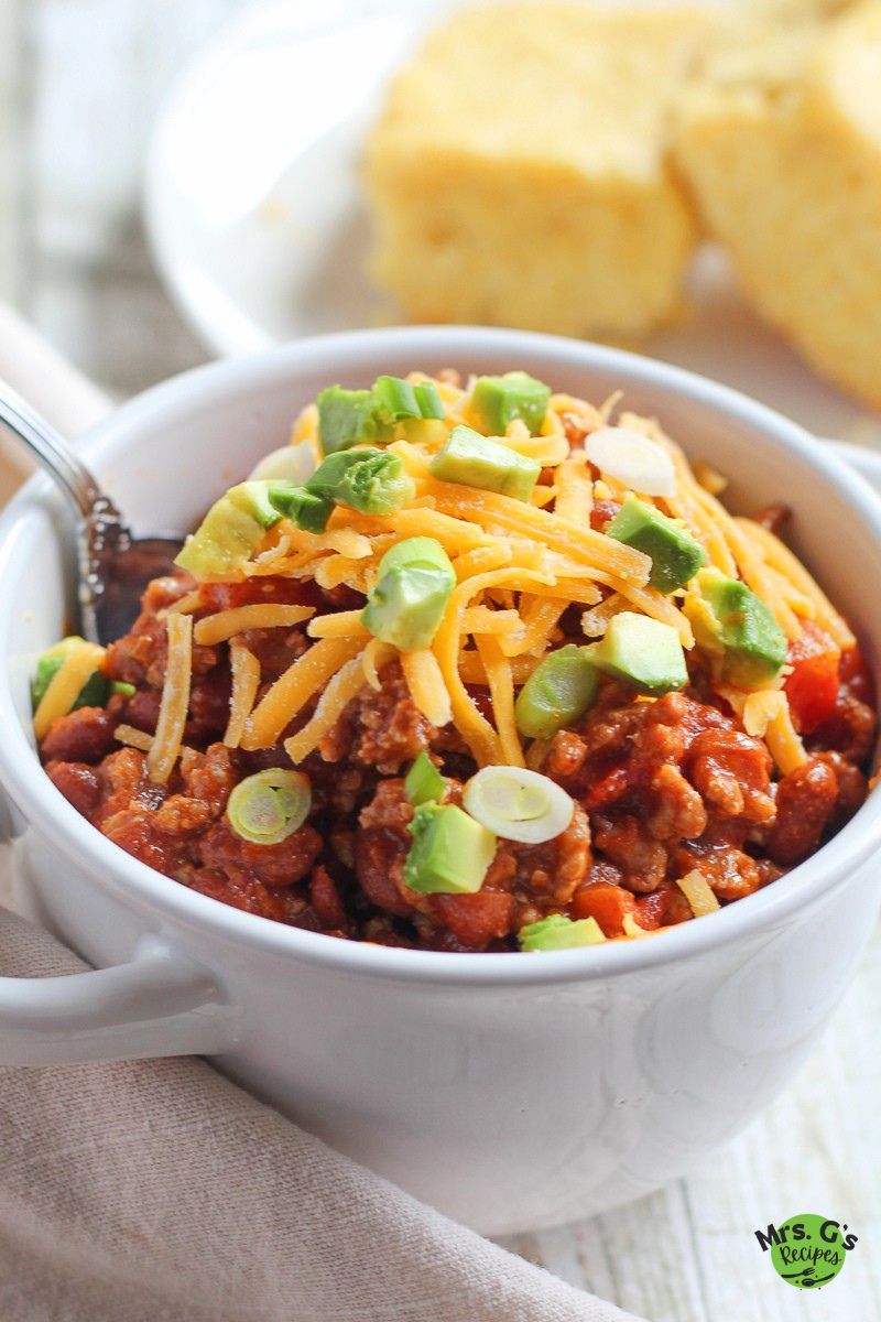 A bowl of chili with cheese and garnish on top.