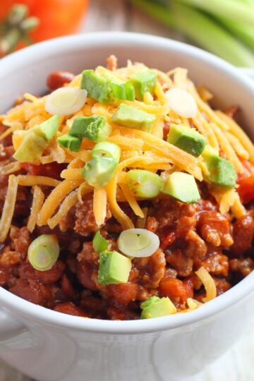 A bowl of chili with cheese and garnish on top.