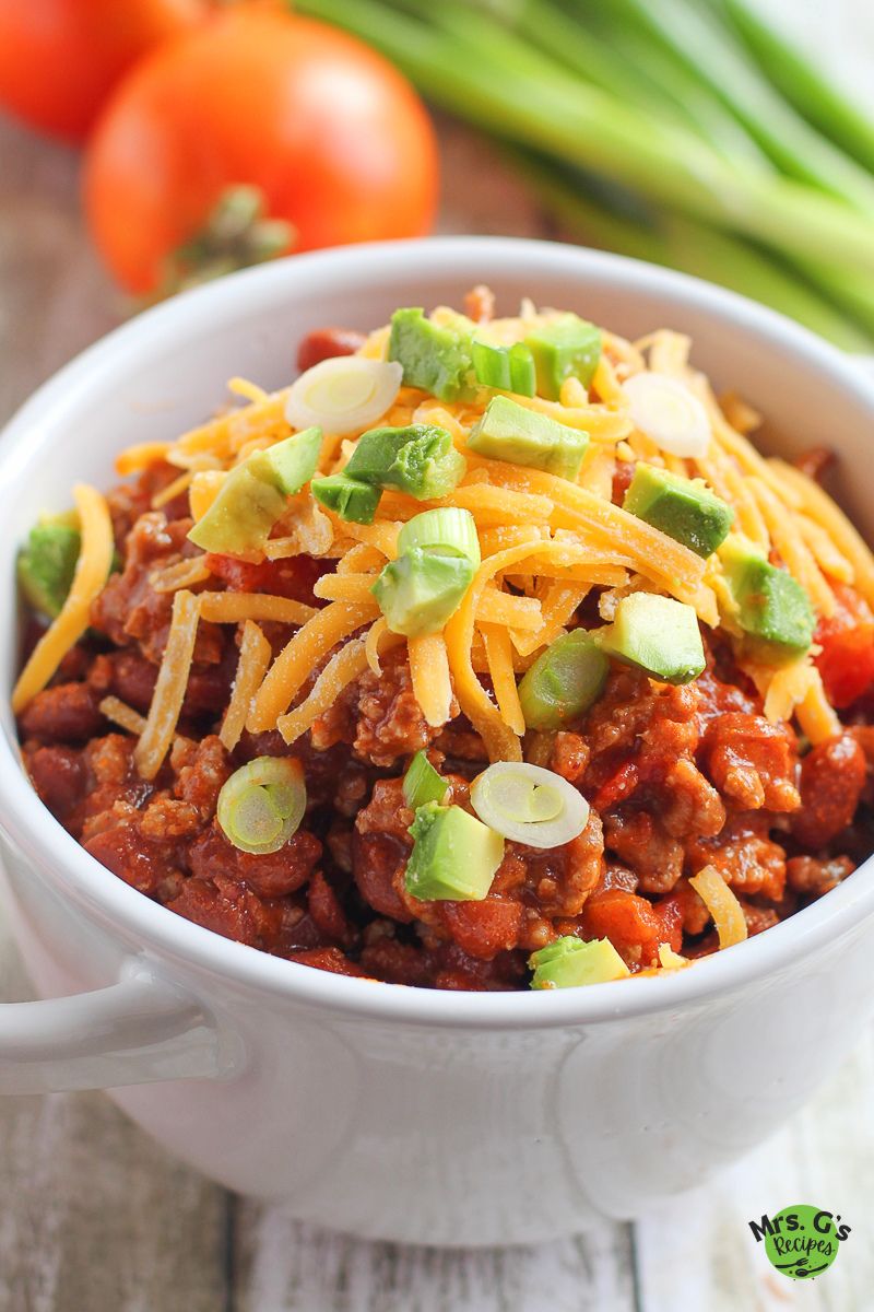 A bowl of chili with cheese and garnish on top.