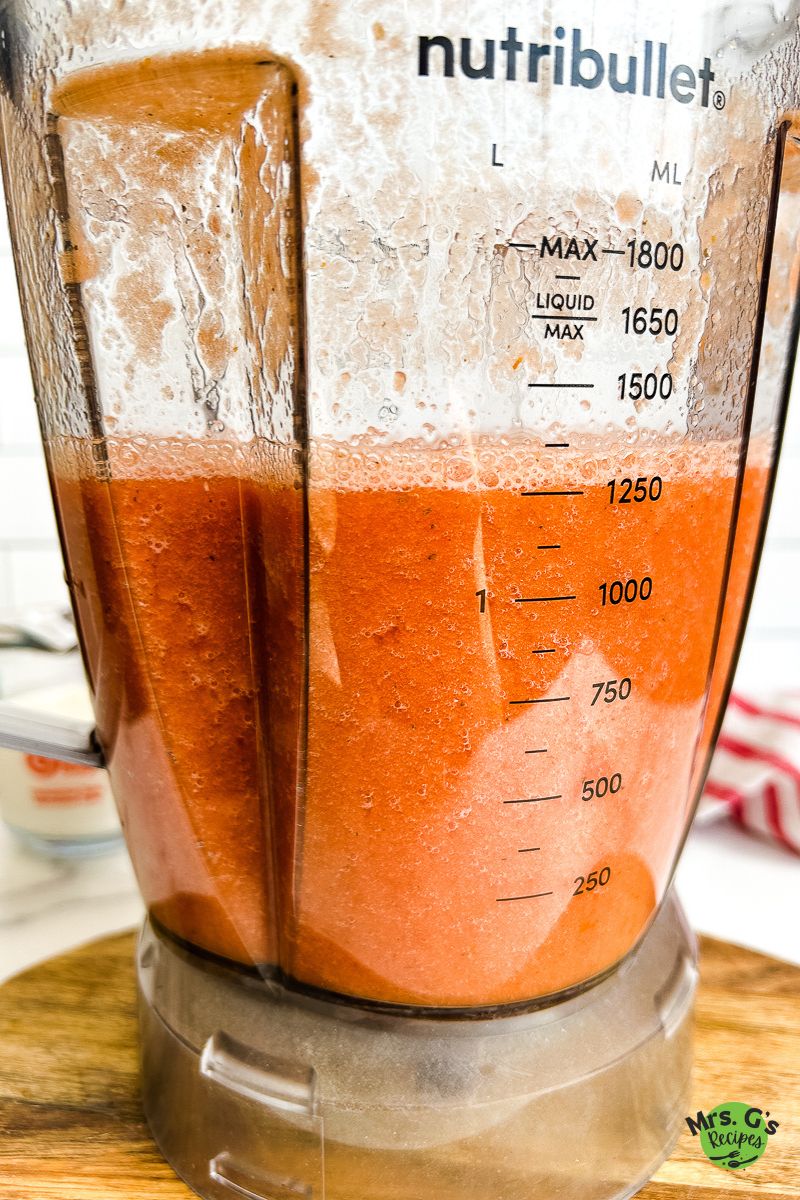 A blender is filled with a creamy, reddish-orange mixture, likely tomato soup, with a Nutribullet logo visible on the side.