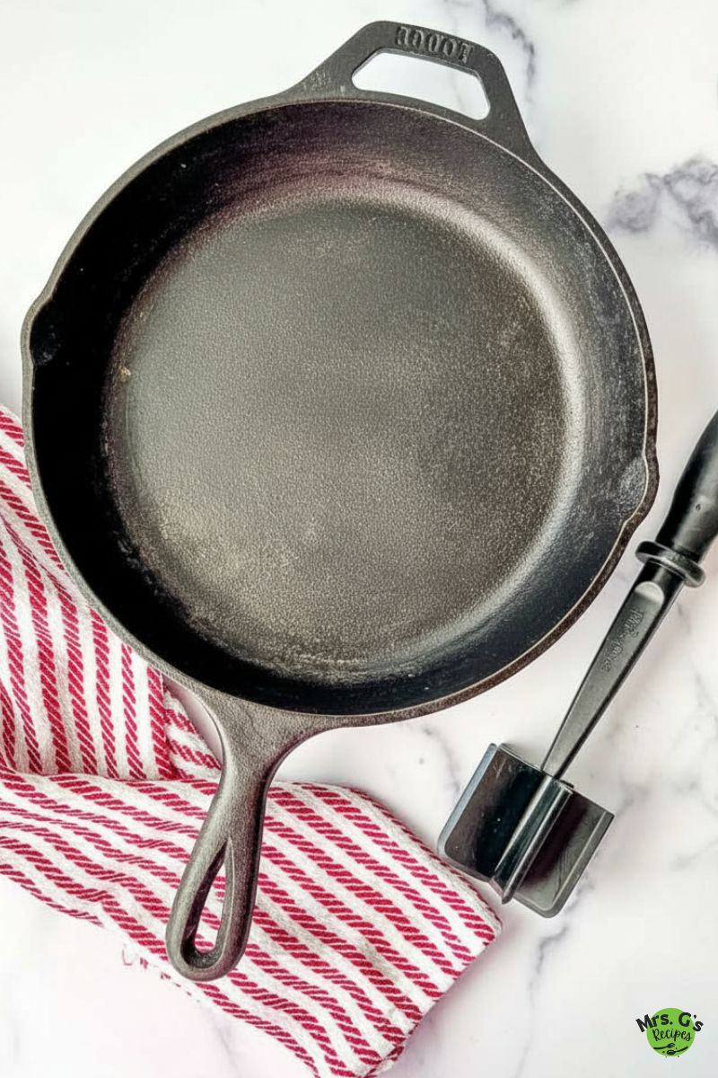 A cast-iron pan with a meat masher and red towel.