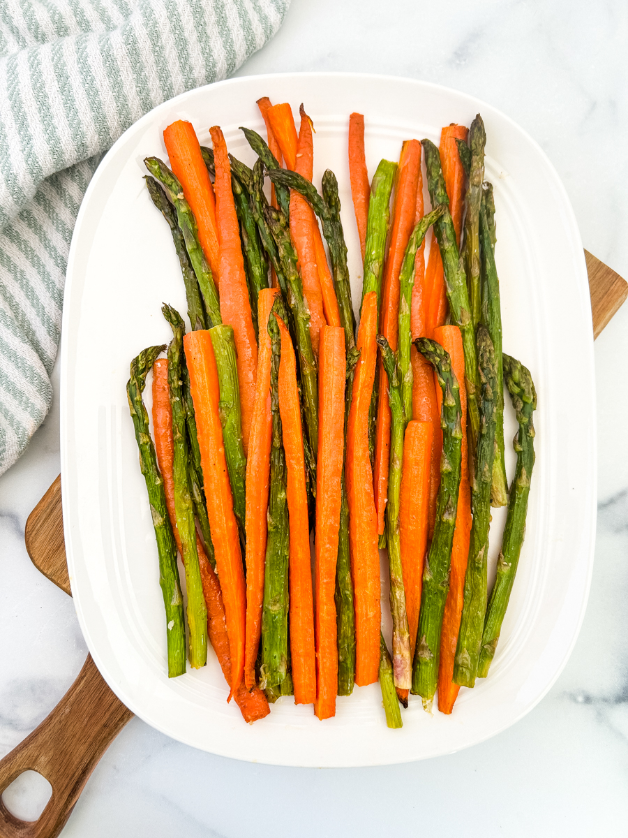 An overhead shot of a large white platter with roasted parmesan carrots and asparagus sprinkled with parmesan.