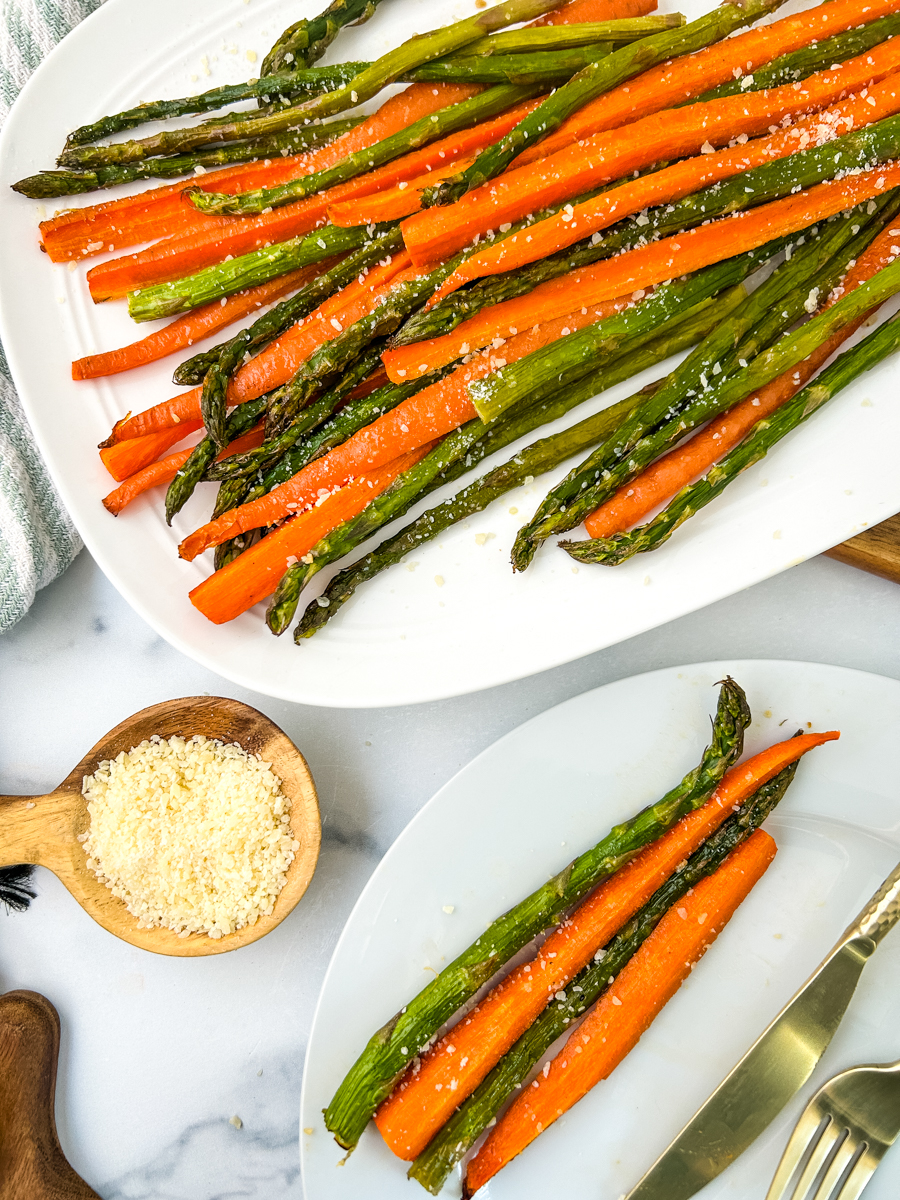 Overhead view of a platter of sliced roasted parmesan carrots and asparagus. There is a small dish of parmesan and a plate with a serving on it.
