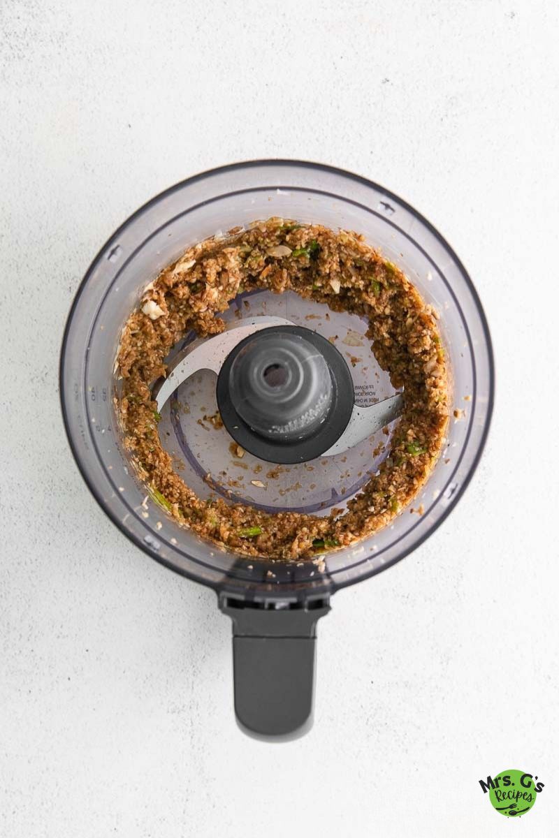 Top-down view into a food processor bowl, showing the finely chopped and seasoned mushroom and vegetable filling for the dumplings.