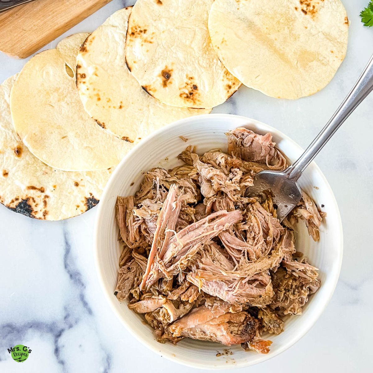 an image of carnitas in Dutch oven recipe with tortillas at the top.