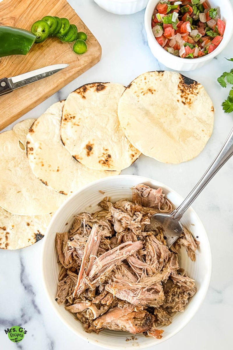a bowl of Dutch oven carnitas with tortilla at the top.