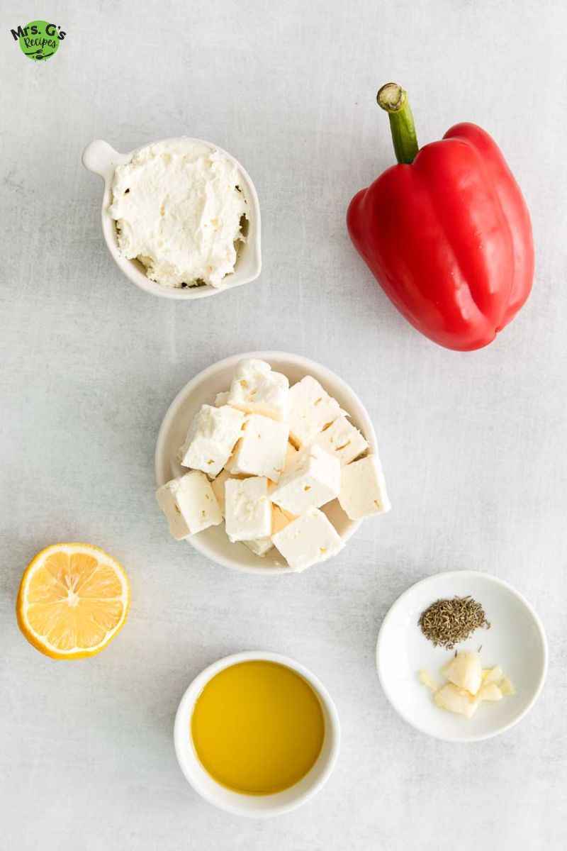 an image of ingredient for feta dip recipe: bell pepper, feta cheese, whipped cream cheese, olive oil, garlic, lemon, and dried thyme.