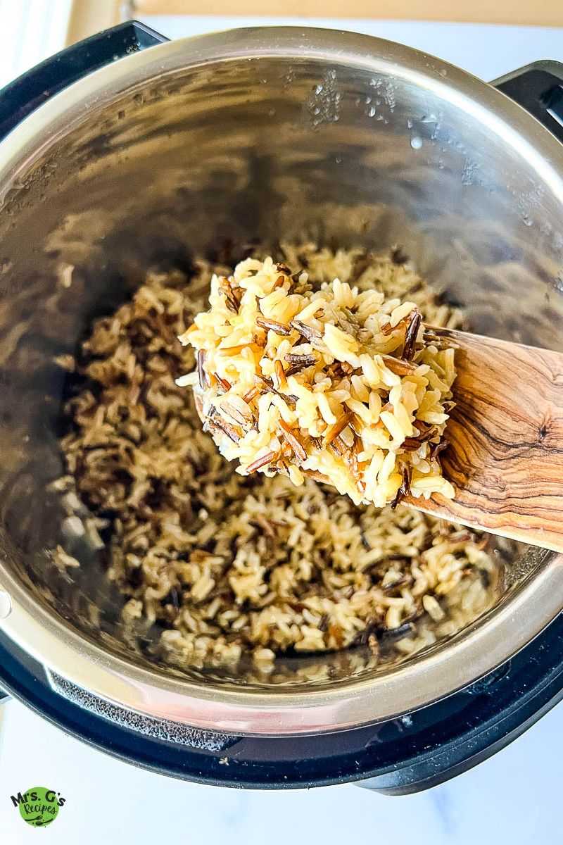 Fluffy cooked grains on a wooden spatula above pressure cooker.