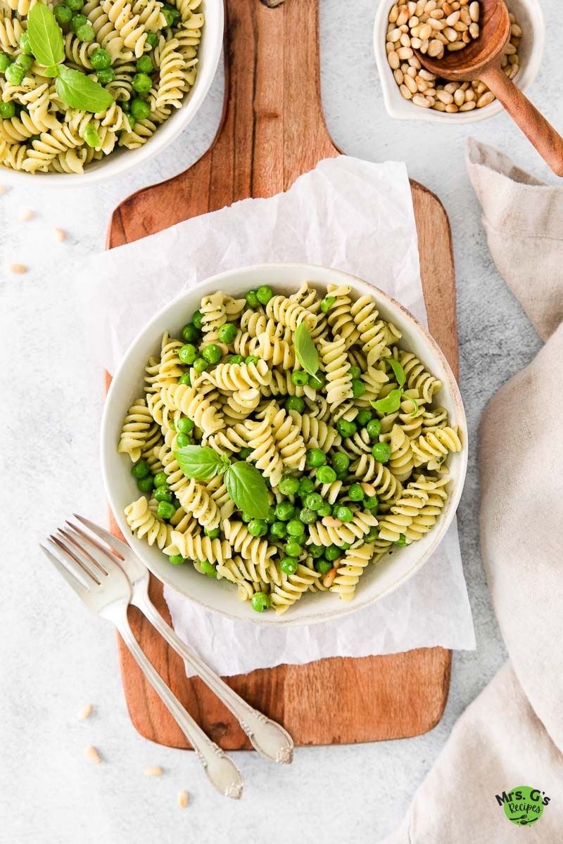 a bowl of pasta and peas with another bowl of pasta and and nuts on the side.