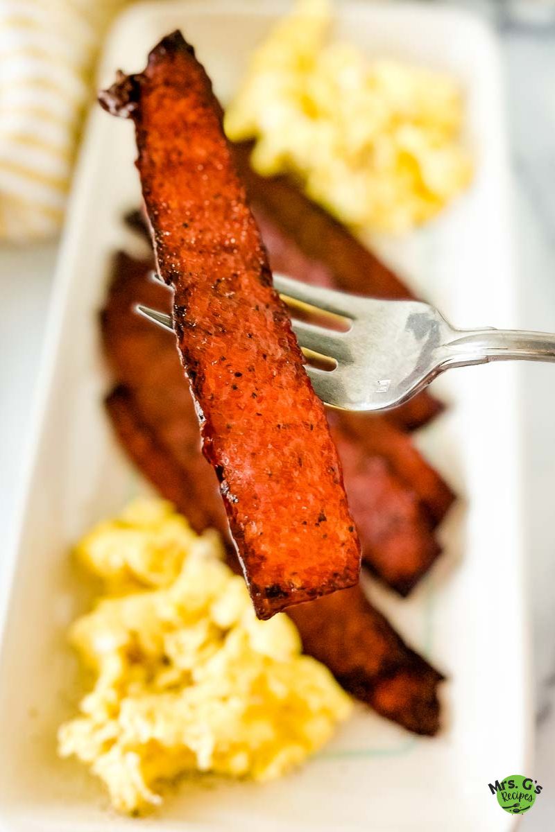 an image of turkey bacon strip with a plate of bacon and egg at the background.