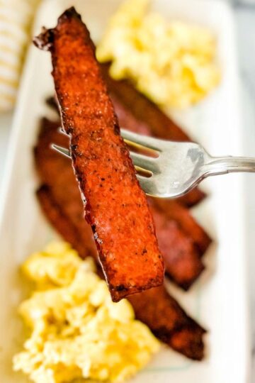 an image of turkey bacon strip with a plate of bacon and egg at the background.
