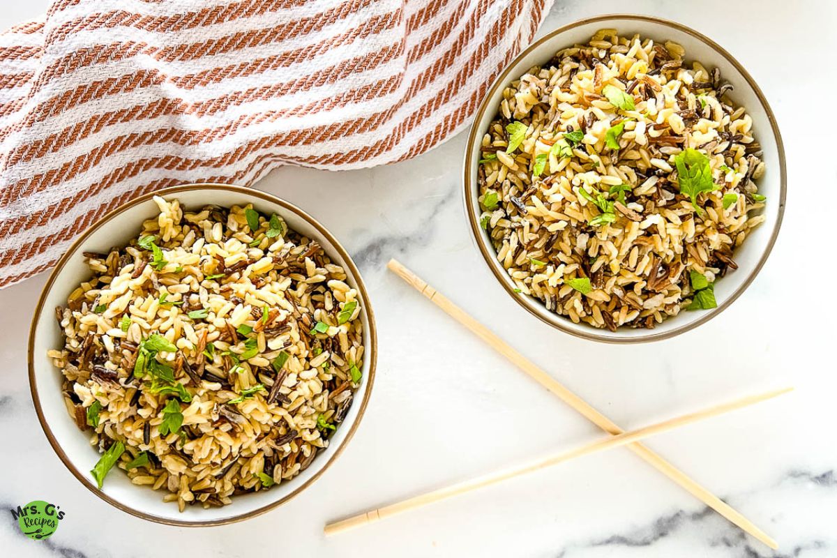 two bowls with cooked Instant Pot wild rice, a chopstick at the center, and a striped red kitchen towel at the side.