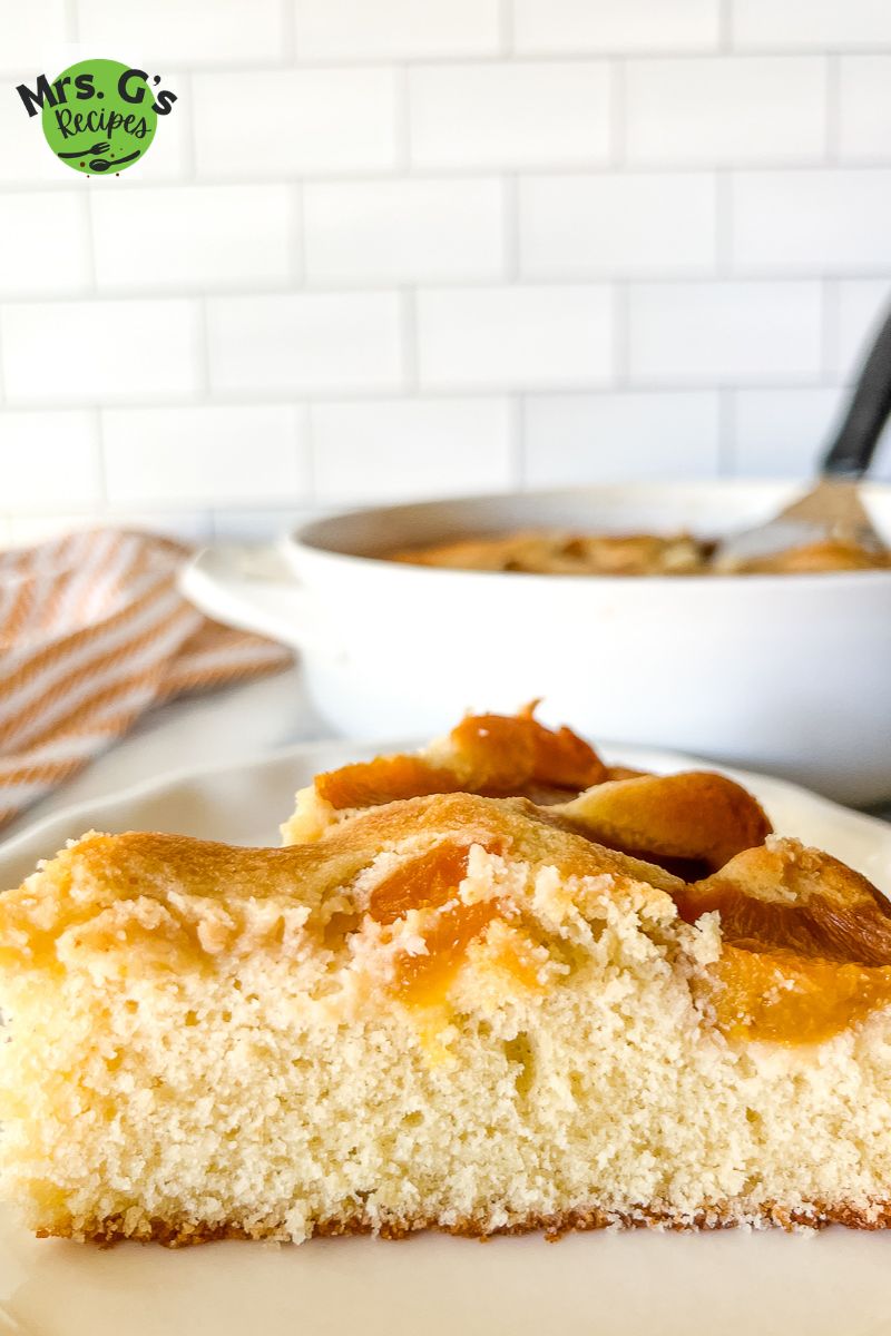 side view: plated slice of moist cobbler cake topped with fresh peaches.