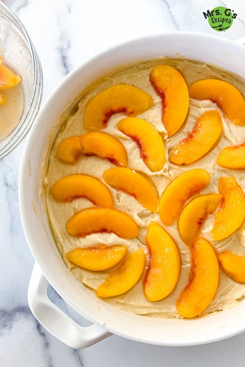 slices of yellow fruit on top of pound cake batter.