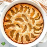 Peach cobbler pound cake baked in a round white baking dish. Stack of dessert plates and spoons sitting behind the pound cake.