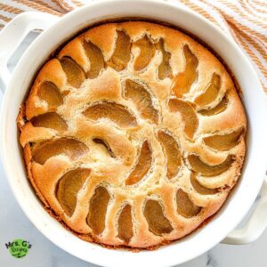 Peach cobbler pound cake baked in a round white baking dish. Stack of dessert plates and spoons sitting behind the pound cake.